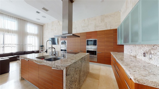 kitchen with light stone counters, sink, a large island with sink, extractor fan, and appliances with stainless steel finishes