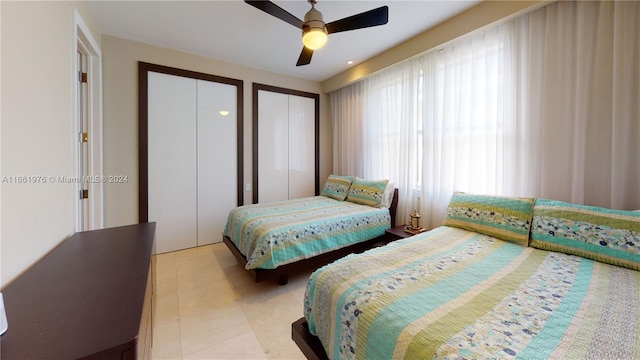 tiled bedroom with ceiling fan and two closets