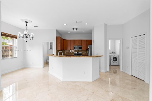 kitchen featuring pendant lighting, appliances with stainless steel finishes, backsplash, a notable chandelier, and washer / clothes dryer