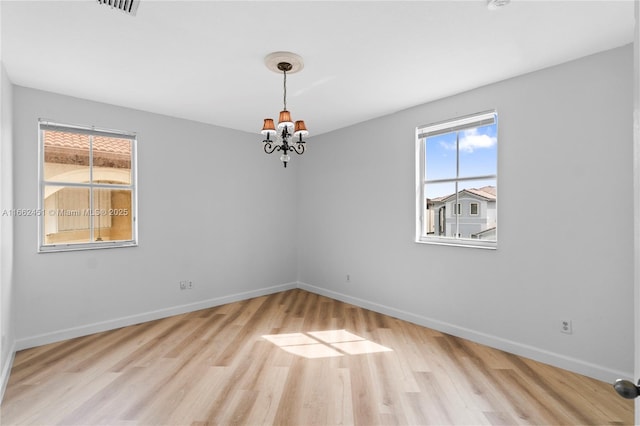 spare room with an inviting chandelier and light hardwood / wood-style floors