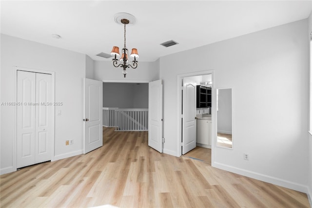 empty room with light wood-type flooring and an inviting chandelier