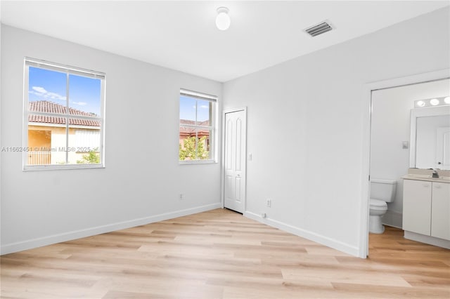 unfurnished bedroom with sink, ensuite bath, and light wood-type flooring