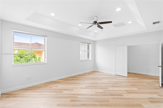 unfurnished room with ceiling fan, a tray ceiling, and light hardwood / wood-style flooring