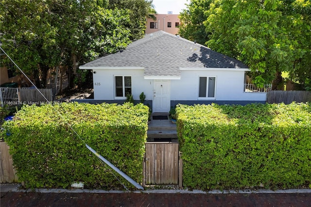 bungalow-style home featuring stucco siding, roof with shingles, and fence