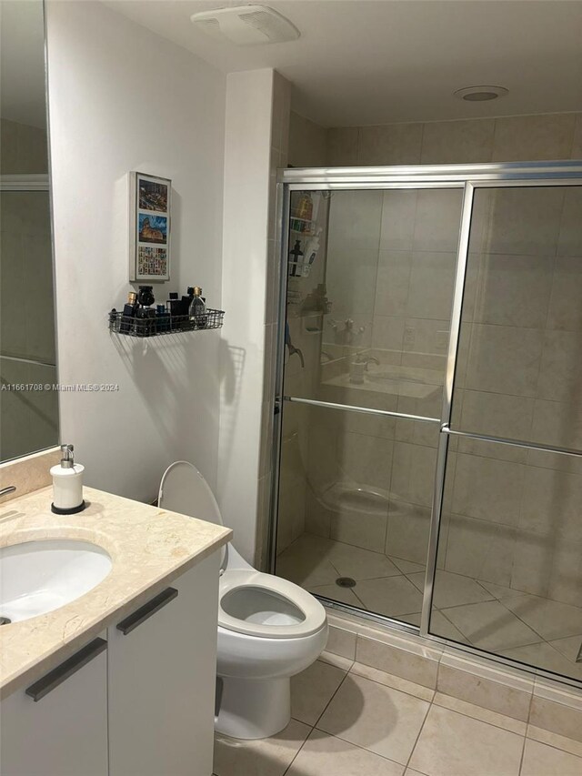 bathroom with vanity, a shower with shower door, toilet, and tile patterned floors