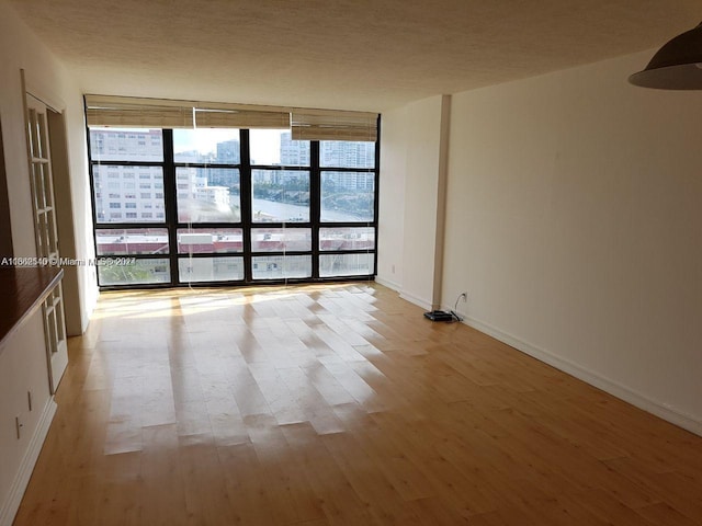 spare room with a textured ceiling, light wood-type flooring, and floor to ceiling windows