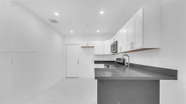 kitchen featuring sink, kitchen peninsula, white cabinetry, appliances with stainless steel finishes, and a breakfast bar