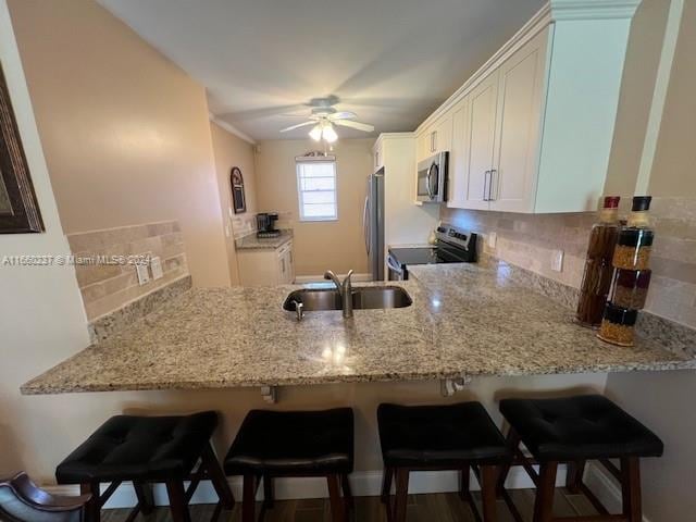 kitchen with white cabinets, kitchen peninsula, stainless steel appliances, ceiling fan, and sink