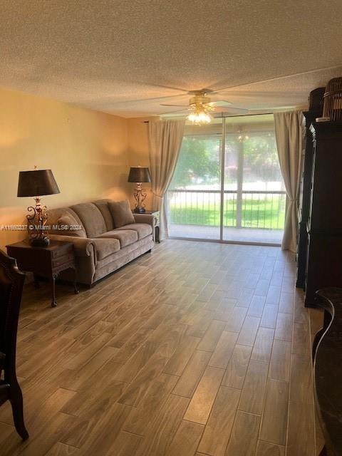 living room featuring wood-type flooring, a textured ceiling, and ceiling fan