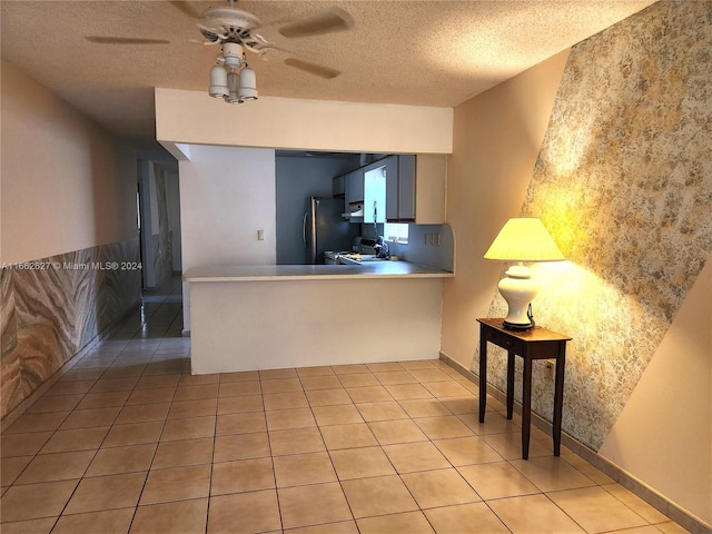 kitchen with ceiling fan, stainless steel fridge, light tile patterned floors, kitchen peninsula, and a textured ceiling