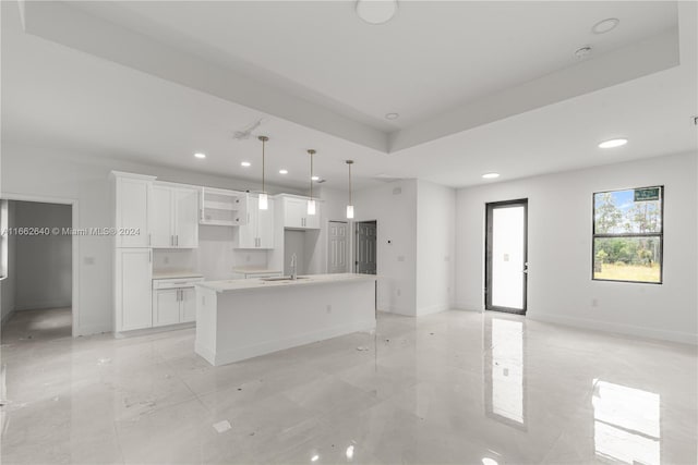 kitchen with a center island with sink, white cabinetry, sink, and decorative light fixtures