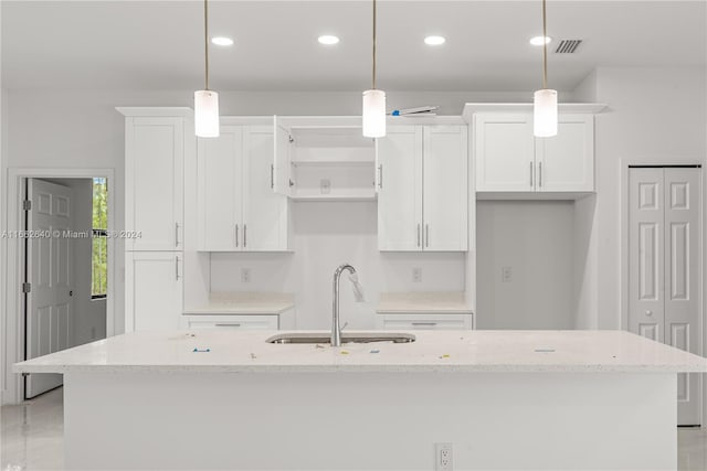 kitchen featuring pendant lighting, white cabinets, a center island with sink, and sink