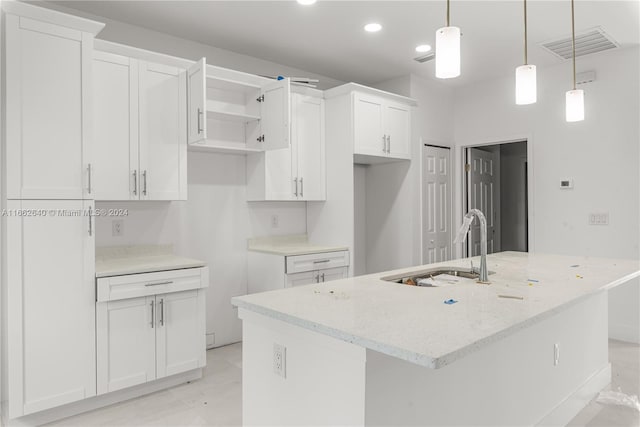 kitchen with sink, an island with sink, white cabinetry, decorative light fixtures, and light stone countertops