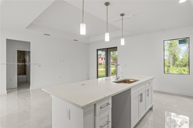 kitchen with hanging light fixtures, a center island with sink, a tray ceiling, and white cabinets