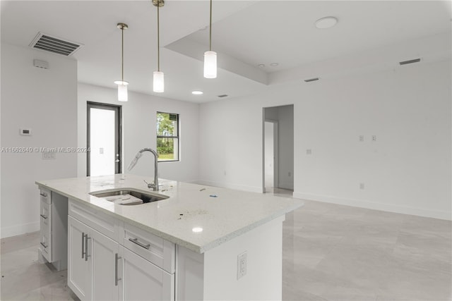 kitchen featuring hanging light fixtures, light stone counters, white cabinets, a center island with sink, and sink