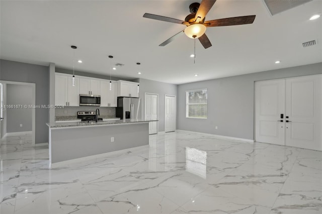 kitchen with appliances with stainless steel finishes, light stone counters, white cabinets, ceiling fan, and a center island with sink