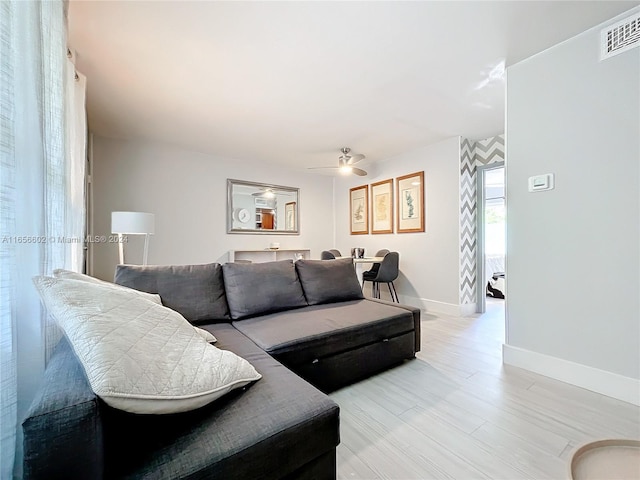 living area with baseboards, light wood-style flooring, visible vents, and a ceiling fan
