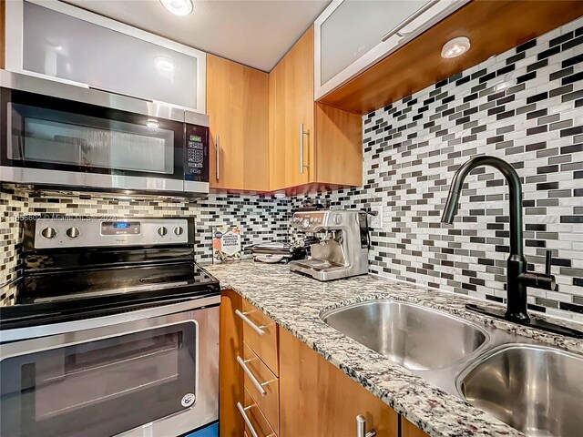 kitchen featuring light stone counters, tasteful backsplash, stainless steel appliances, and a sink