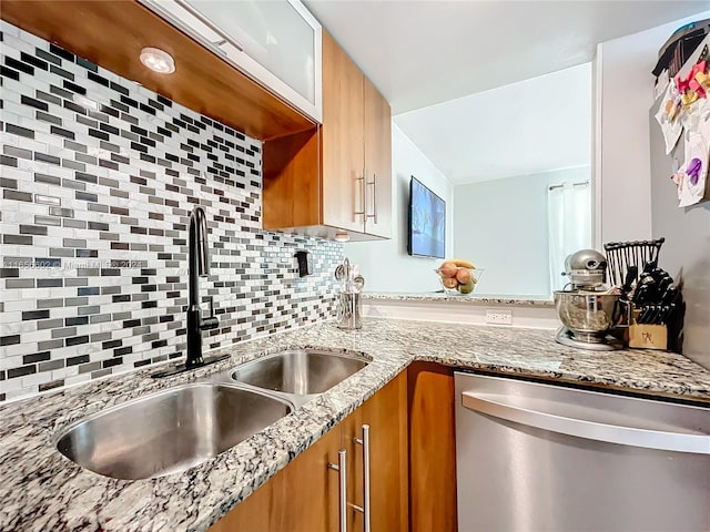 kitchen featuring a sink, brown cabinetry, decorative backsplash, dishwasher, and light stone countertops