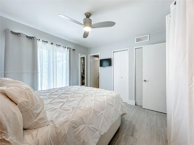 bedroom featuring baseboards, visible vents, wood finished floors, ceiling fan, and two closets