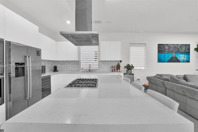 kitchen featuring white cabinets, wine cooler, island range hood, backsplash, and appliances with stainless steel finishes