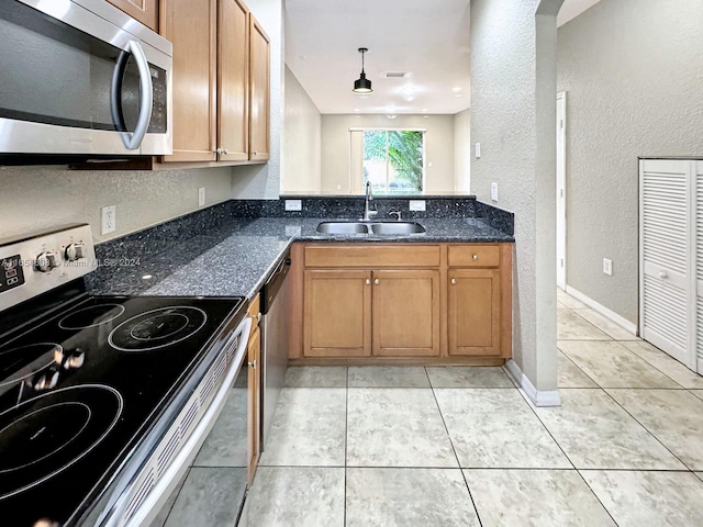 kitchen with dark stone countertops, light tile patterned floors, appliances with stainless steel finishes, and sink