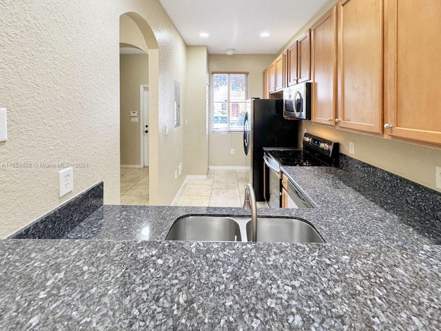 kitchen with light tile patterned floors, appliances with stainless steel finishes, sink, and dark stone counters