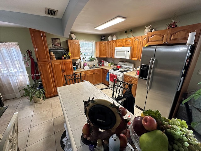 kitchen featuring white appliances, light tile patterned floors, visible vents, arched walkways, and brown cabinets