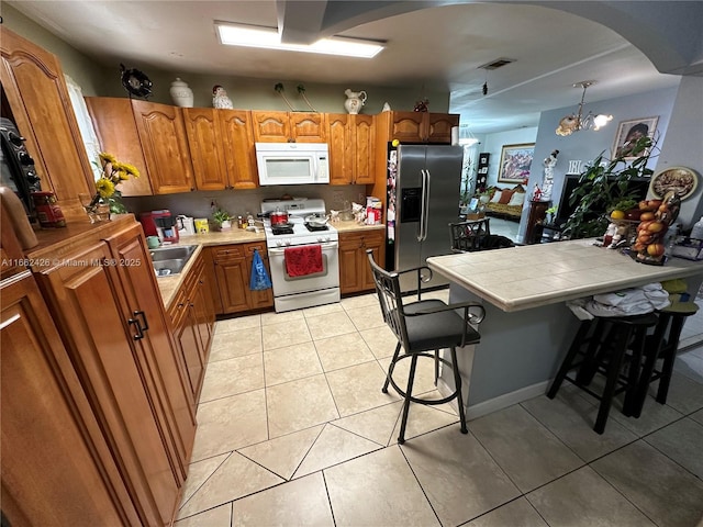 kitchen with light tile patterned floors, white appliances, a sink, visible vents, and brown cabinets