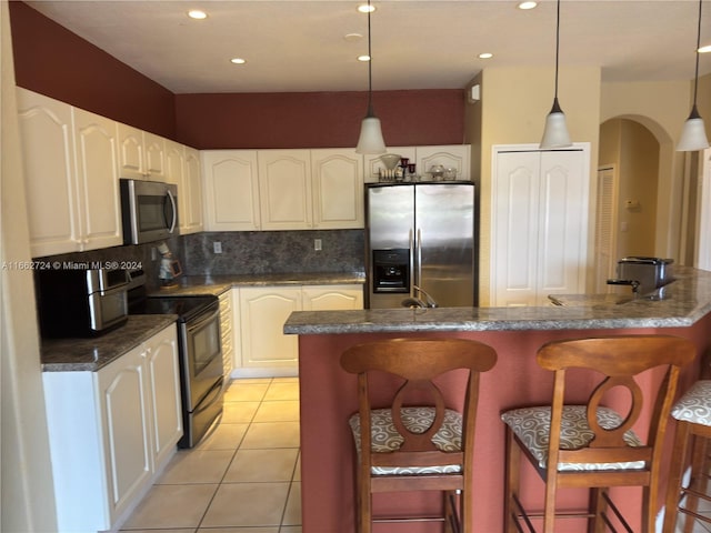 kitchen with a center island with sink, stainless steel appliances, hanging light fixtures, and a kitchen bar