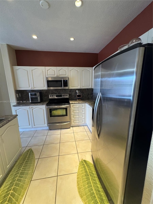 kitchen with decorative backsplash, white cabinets, appliances with stainless steel finishes, and light tile patterned floors