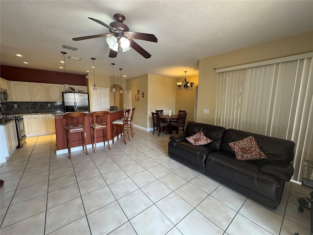 living room with ceiling fan with notable chandelier, a textured ceiling, and light tile patterned floors