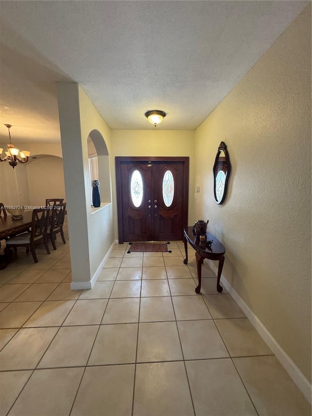 foyer featuring a textured ceiling, light tile patterned flooring, and an inviting chandelier