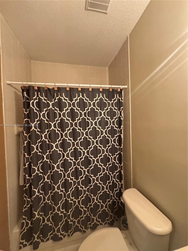 bathroom featuring a textured ceiling, curtained shower, and toilet