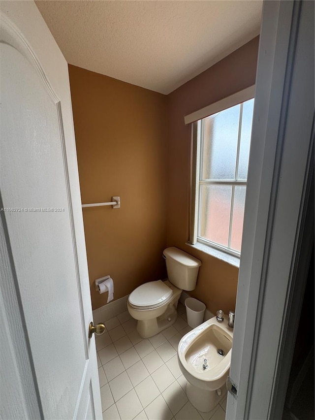 bathroom featuring a textured ceiling, tile patterned flooring, toilet, and a bidet