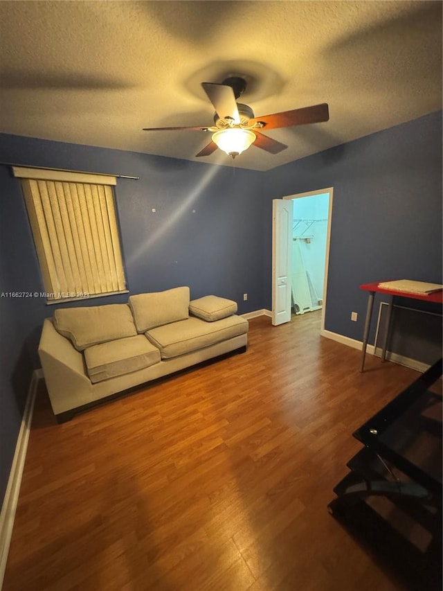 living room featuring ceiling fan, a textured ceiling, and wood-type flooring