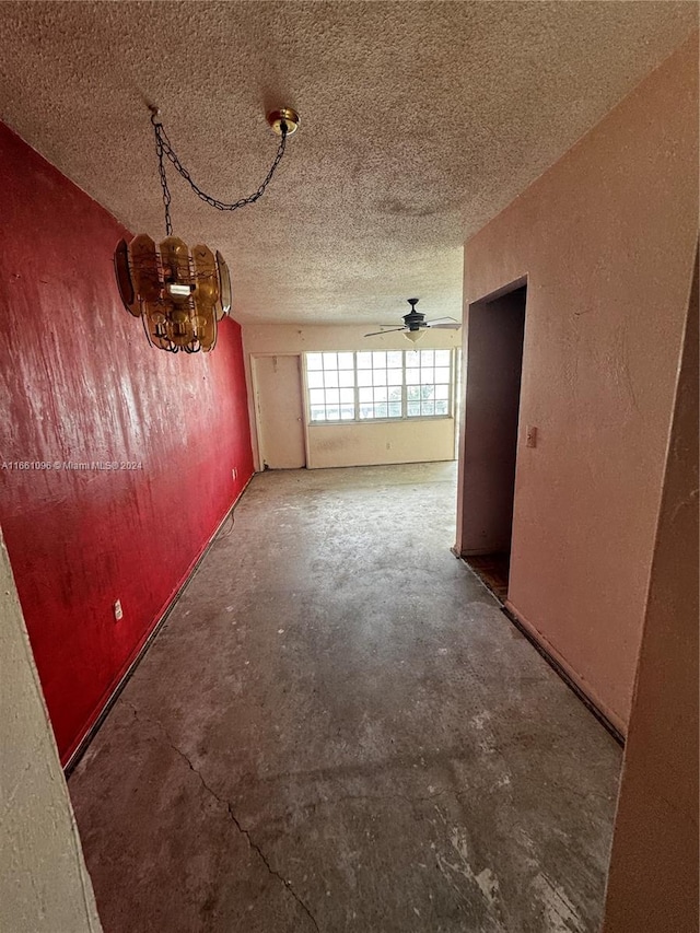 empty room featuring a textured ceiling, ceiling fan with notable chandelier, and concrete floors