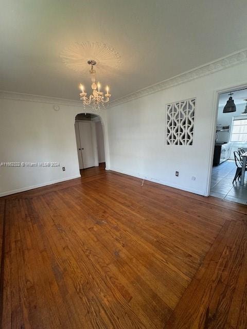 empty room featuring ornamental molding, a notable chandelier, and dark hardwood / wood-style flooring