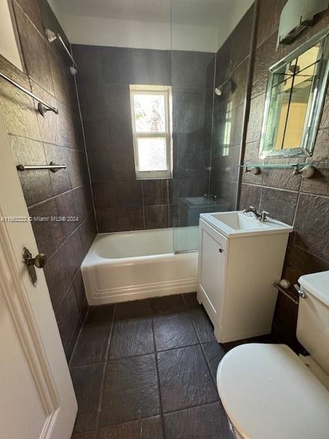 full bathroom with tile walls, tiled shower / bath, vanity, and toilet