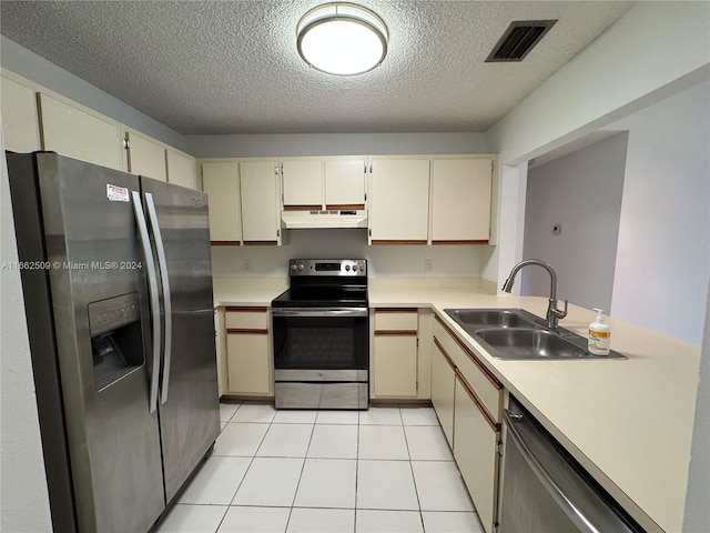 kitchen with sink, a textured ceiling, cream cabinetry, light tile patterned flooring, and stainless steel appliances