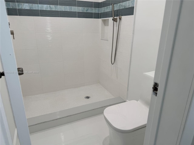 bathroom featuring tile patterned flooring, toilet, and a tile shower