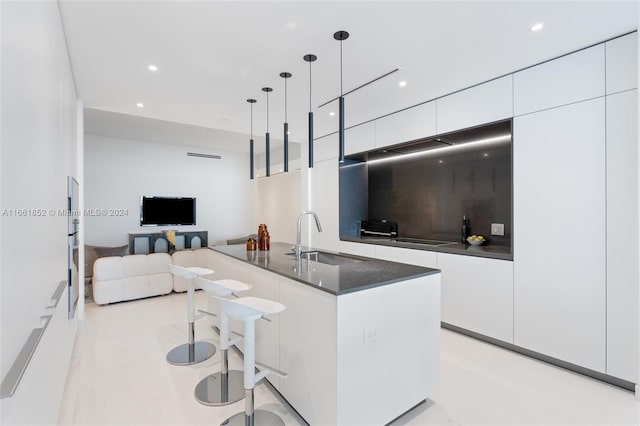 kitchen featuring a breakfast bar, decorative light fixtures, white cabinetry, sink, and a center island