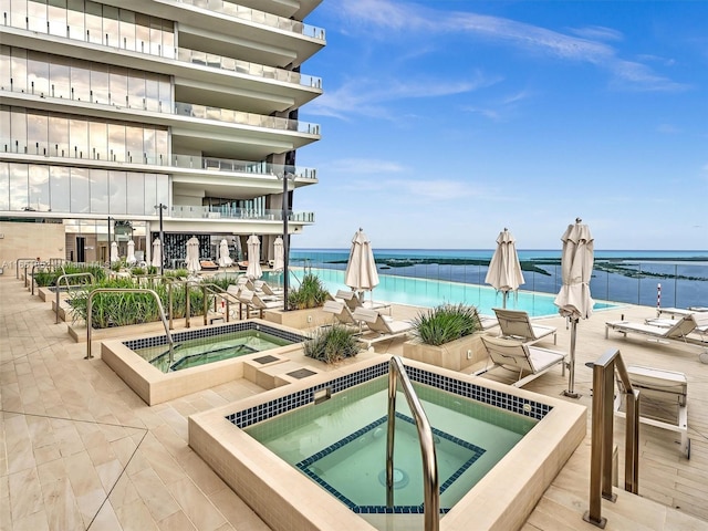 view of swimming pool featuring a water view, a hot tub, and a patio area