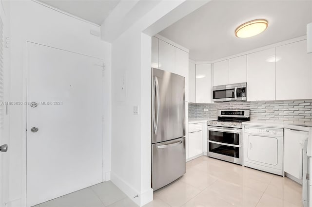 kitchen featuring light tile patterned flooring, backsplash, white cabinetry, appliances with stainless steel finishes, and washer / dryer