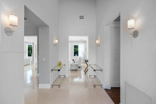 hall featuring a towering ceiling, baseboards, and visible vents