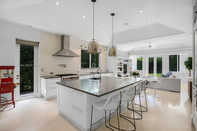 kitchen with white cabinetry, wall chimney range hood, decorative backsplash, decorative light fixtures, and ceiling fan