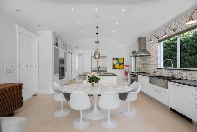 kitchen with a kitchen island with sink, tasteful backsplash, white cabinets, wall chimney range hood, and decorative light fixtures