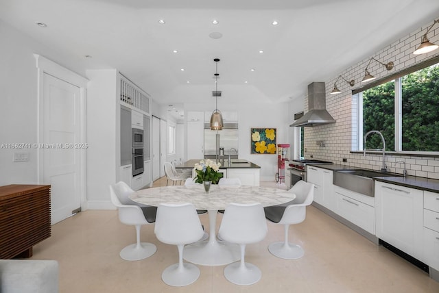 kitchen featuring a center island with sink, wall chimney exhaust hood, a sink, stainless steel appliances, and backsplash