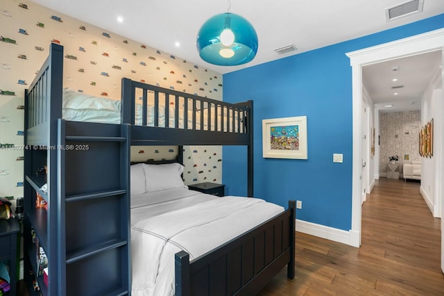 bedroom featuring baseboards, wood finished floors, visible vents, and wallpapered walls