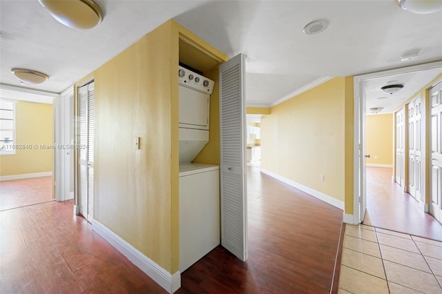 corridor featuring wood-type flooring, stacked washer and dryer, and ornamental molding